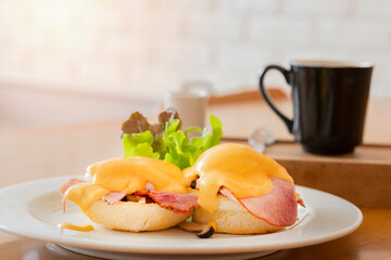 Egg Benedict consisting of two English muffins and topped with Canadian bacon, a poached egg and hollandaise sauce, American breakfast or brunch dish, serving with vegetable and hot black coffee