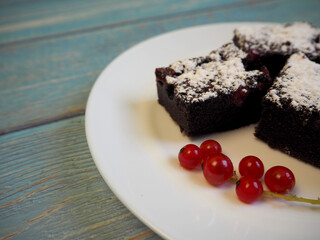 three pieces of gluten-free chocolate cakes with red currants, sprinkled with powdered sugar, lie on a white plate on a blue table. gluten-free cakes. homemade cakes with a diet