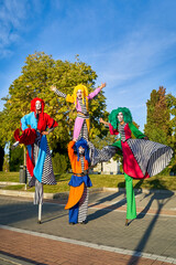 Funny stilt walkers in multicolored costumes standing in park during parade