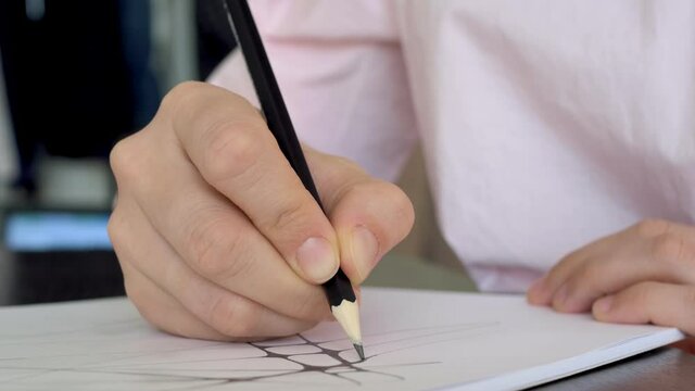 Artist work on paper using a pencil. The designer draws a sketch on paper. Close-up of a pencil in hand which draws lines on a sheet of paper. Neurography and therapy.