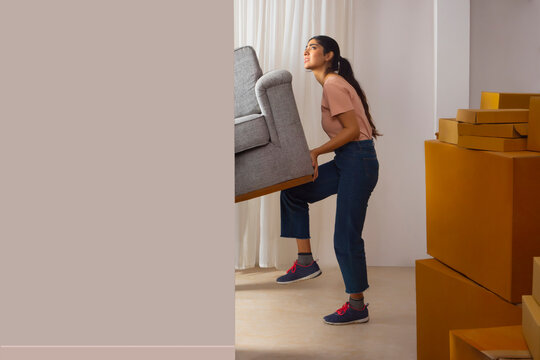 Adult girl lifting sofa and trying to move