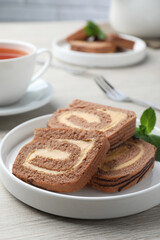 Tasty chocolate cake roll with cream and mint on light wooden table