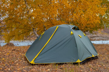 Green tent near river with colorful mountain forest in autumnseason. Autumn nature landscape. Tourism, trekking in fall season concept. Nature of Dzungarian Alatau in Kazakhstan.