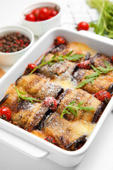 Tasty eggplant rolls with tomatoes, cheese and arugula in baking dish on white table, closeup