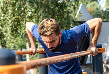 Fitness motivation. A thin man is trying to do push-ups on the uneven bars.