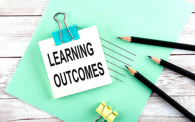 Text LEARNING OUTCOMES on the short note with pencils on wooden background