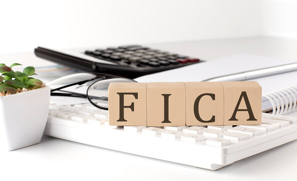 FICA written on a wooden cube on keyboard with office tools