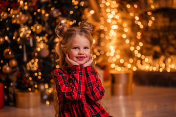 beautiful little girl in a red dress at home near the tree opens gifts