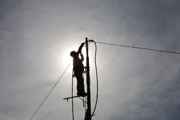 an electrician climbs a power pole to connect electrical wires to make a new electrical connection