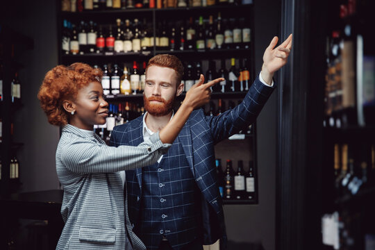 Lover multicultural couple talking and choosing wine in shop. Man and African girl are buying alcohol