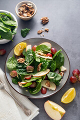 Healthy salad with red apple, wallnuts, grapes and fresh spinach leaves. Dark background