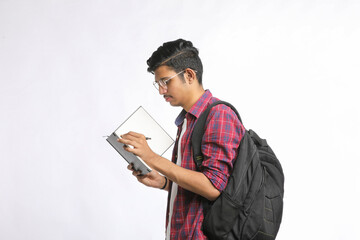 Indian college student standing with bag and reading dairy over white background.