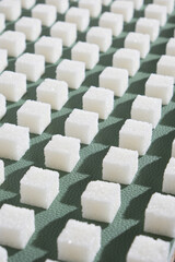 Refined sugar on green background.Cubes of sweet and white sugar in geometricshape. Hard shadows.