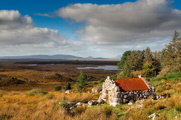 Fototapeta na wymiar Small stone building with rusty red metal roof with beautiful nature scenery in the background. Connemara area, county Galway, Ireland. Storage hut in a field. Historical building. Cloudy sky