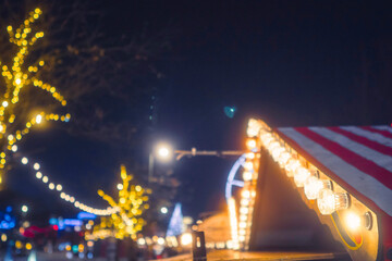 Scene at a Winter Christmas market. Lights on a small shop in focus. Illuminated park out of focus. Festive season. Magic time of the year.