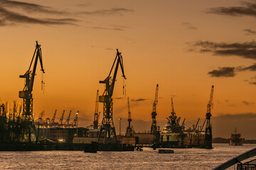 Fototapeta na wymiar View to the river Elbe in Hamburg with cranes, dock and super-yacht after sunset with afterglow