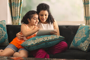 Mother and daughter using tablet together while sitting on sofa at home