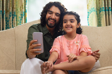 Father taking selfie with her daughter while sitting on sofa at home