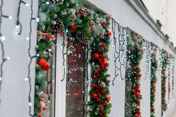 Christmas shop windows. Fir garland decorated with red balls, berries, cones and lights