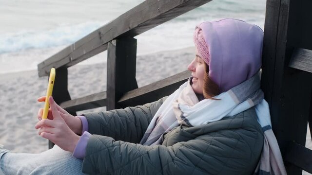Woman blogger in warm clothes does selphie on the winter beach. Traveller at the cold sea in the off-season, 4k 60p