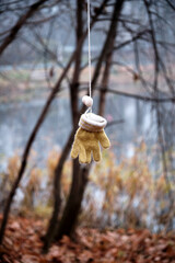 A child's glove with pompoms hangs on a blurry natural background. Vertical image. Autumn mood