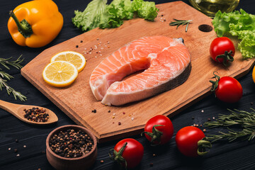 Dietary festive lunch, dinner. Salmon. Steak of fresh raw fish with tomatoes, lemon, pepper and herbs on a wooden board and a dark background. Top and side view. Wellness.