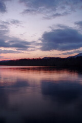 Fototapeta na wymiar 淡い色合いの夜明けの空を湖面に反射する湖。