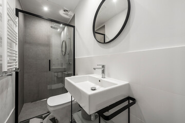 Modern design shower toilet in white, black and gray colors with round mirror and white wall mounted radiator
