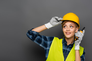 Blonde builder in safety vest holding walkie talkie on grey background
