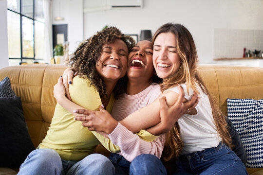 Three happy friends hugging smiling.Funny women together celebrating sitting on the living room sofa