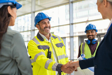 Mature architect and contractor shaking hands at construction site - obrazy, fototapety, plakaty
