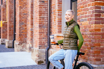 Fototapeta na wymiar Beautiful middle age laughing blonde short hair hipster woman with bike in the city.