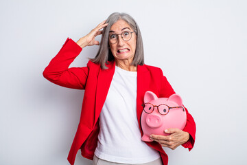 senior pretty woman feeling stressed, anxious or scared, with hands on head. piggy bank concept