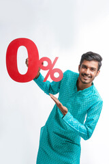 Indian man holding zero percent sign board promoting offers on festival season while wearing traditional cloths, standing over white background.