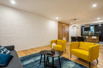 Living room with exposed white brick walls and contemporary decor with yellow individual armchairs and black coffee table