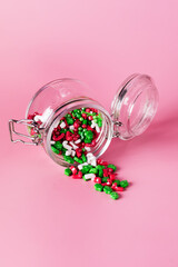 Glass Jar with Christmas Candy Sprinkles on Pink Background Vertical