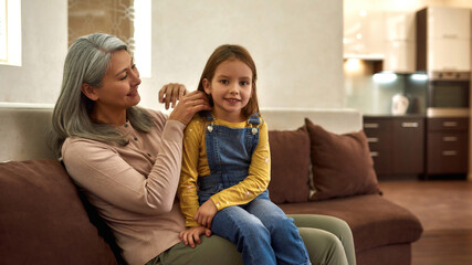 Photo of two people, aged granny and young granddaughter sitting on cozy sofa