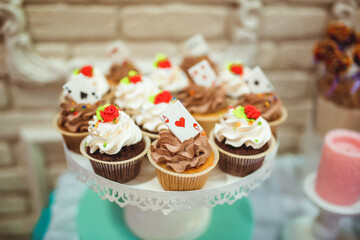 white cream cupcakes decorated with cherry and cards made of caramel on white tray against blurred background