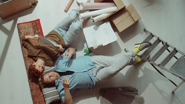 Top down shot of man and woman lying on floor among home renovation supplies and discussing interior design