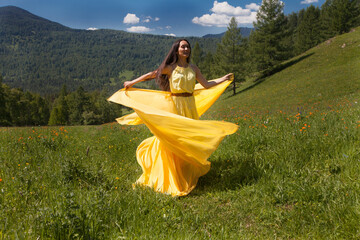 A beautiful woman of Asian appearance in a yellow dress walks in the summer in Altai.