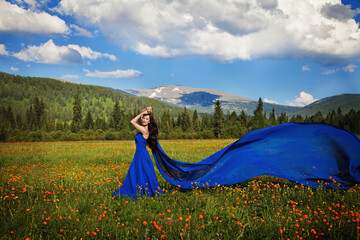 A beautiful woman of Asian appearance in a blue dress walks in a green meadow with orange flowers in the Altai mountains in summer. concept beauty, tourism.
