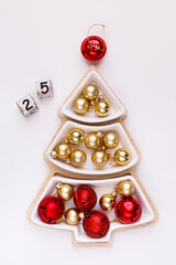 New Year's Eve white Christmas tree-shaped plate on a wooden tray with red and gold balls and dice with the number 25. New Year's concept with room for text