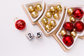 New Year's Eve white Christmas tree-shaped plate on a wooden tray with red and gold balls and dice with the number 25. New Year's concept with room for text