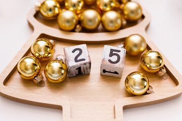 New Year's Eve white Christmas tree-shaped plate on a wooden tray with gold balls and dice with the number 25. New Year's concept with room for text
