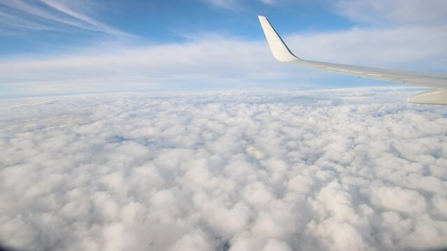 Travel by plane with white clouds and blue horizon, wing of the plane in the foreground. Panorama from the window of an airliner in flight for tourism. Blue sky with clouds and airplane flight