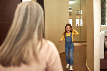 Back view elder woman welcoming little girl at home