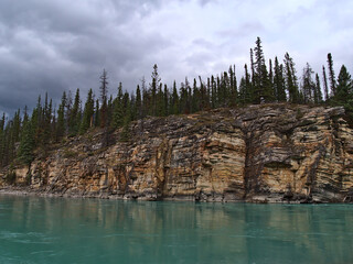 View of colorful eroded rock face with visible layers at Athabasca River in Jasper National Park, Alberta, Canada in the Rocky Mountains with trees.
