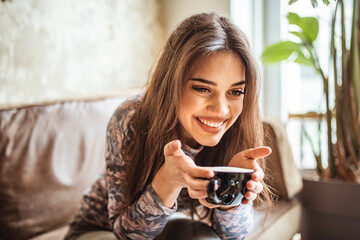 Stylish young woman drinking coffee at the cafe, looking away. Happy woman enjoying in cup of fresh coffee. Smiling calm young woman drinking coffee. Shot of an attractive young woman relaxing at cafe
