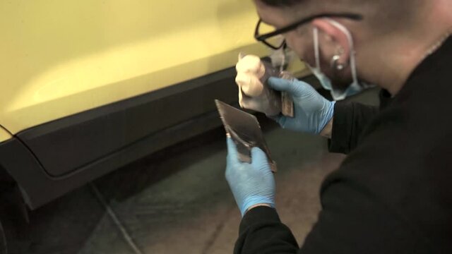 Auto mechanic repairing a yellow car with putty for paint in a workshop
