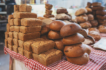 Pile of freshly baked loaves of bread on table at the local market. Many traditional fresh round and square bread loaves for sale. No people. Selective focus.